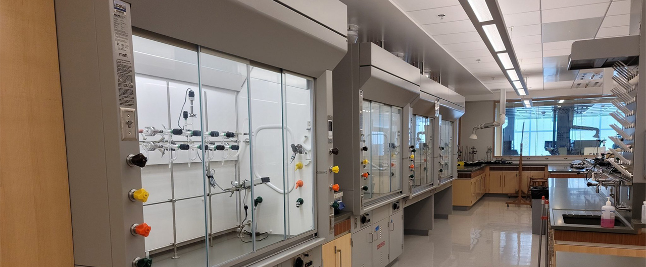 Some fume hoods in a lab. The hoods are enclosed work stations, several feet across and several feet wide, with pipes and other equipment inside of a glass window.